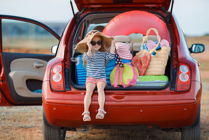 Little girl in straw hat sitting in the trunk of a car