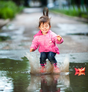 happy little girl, wearing a pink jacket,  jumps into a puddle