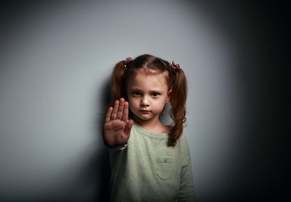 Kid girl showing hand signaling to stop useful to campaign against violence and pain on dark background with empty copy space