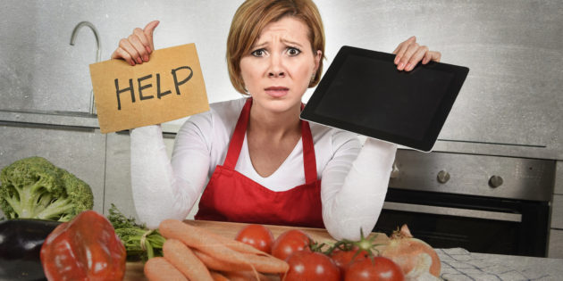 inexperienced home cook woman in red apron screaming desperate and frustrated at domestic kitchen in stress holding digital tablet asking for help in amateur and rookie cooking mess