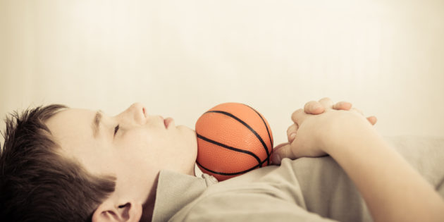 Side profile view on single cute child asleep with little basketball under chin and folded hands on chest
